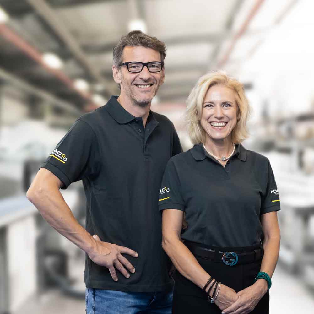 Two HOAC employees stand next to each other in work clothes and smile at the camera