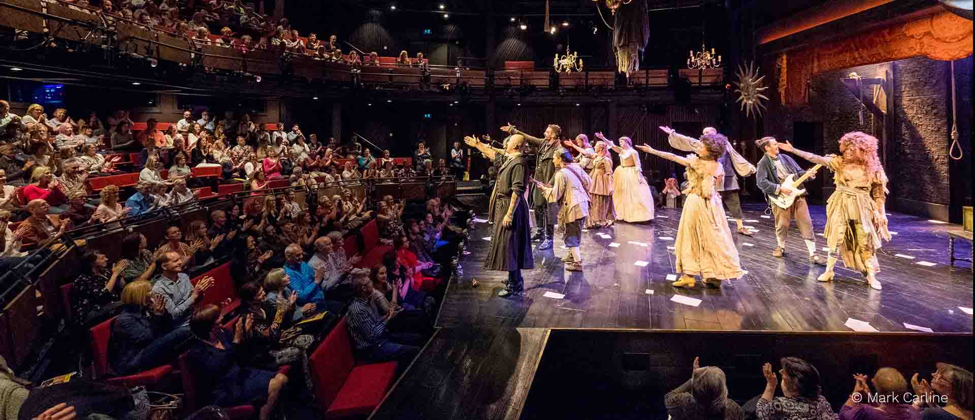 Several people performing a play on a theater stage in front of an audience