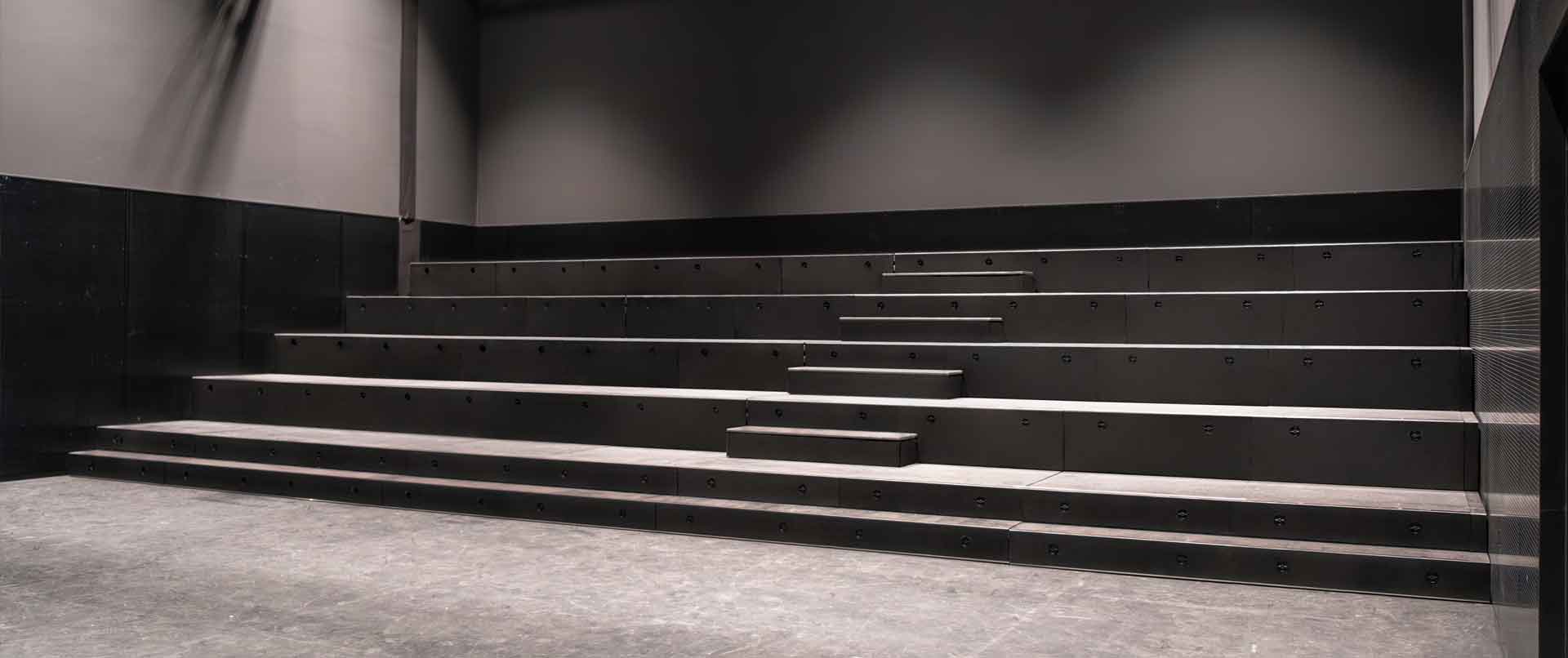 Leere schwarze Zuschauertribüne in einem minimalistischen Saal mit schlichten Details.